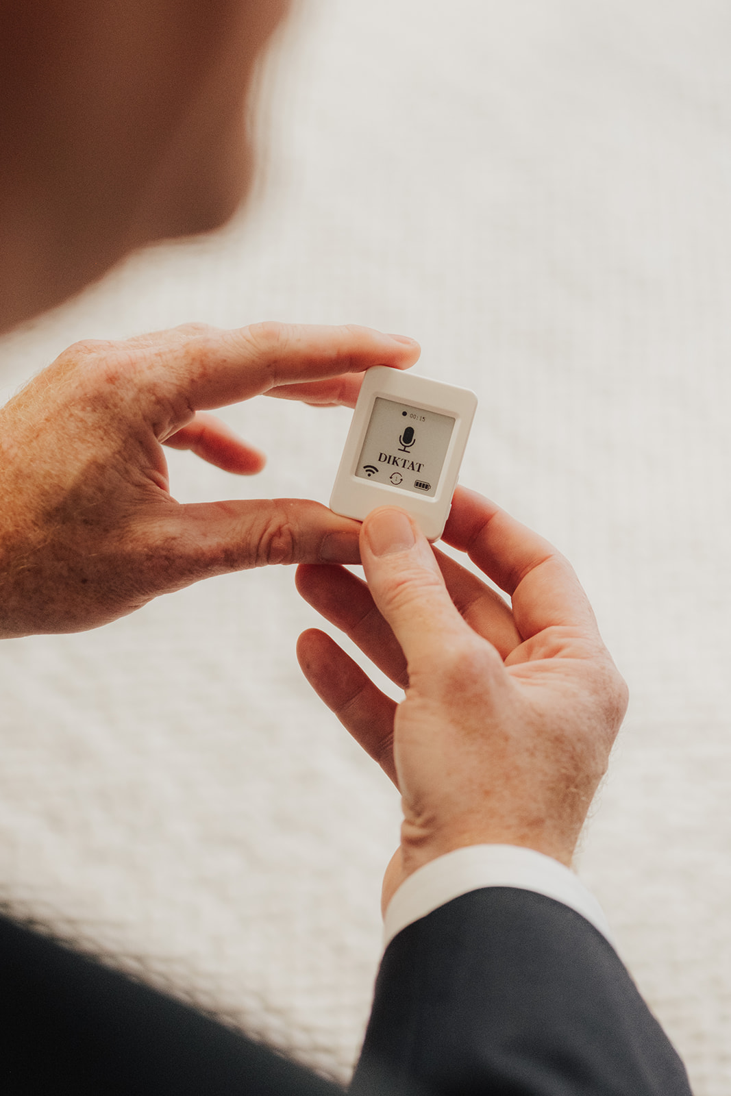 Das IURIX DIXI Pocket Diktiergerät frontal in Händen gehalten — das E-Paper-Display zeigt DIKTAT mit Mikrofon-Symbol und WLAN-Icon.